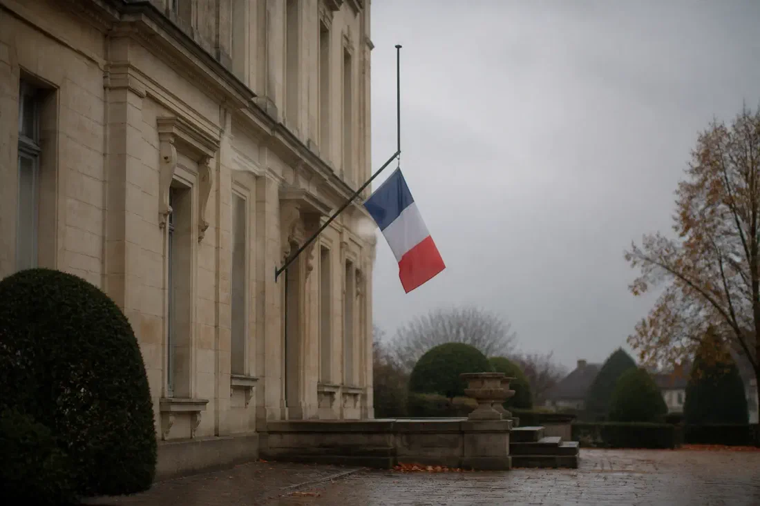 Illustration générée par IA d'un drapeau français en berne sur la façade d'une mairie, sous un ciel gris d'automne