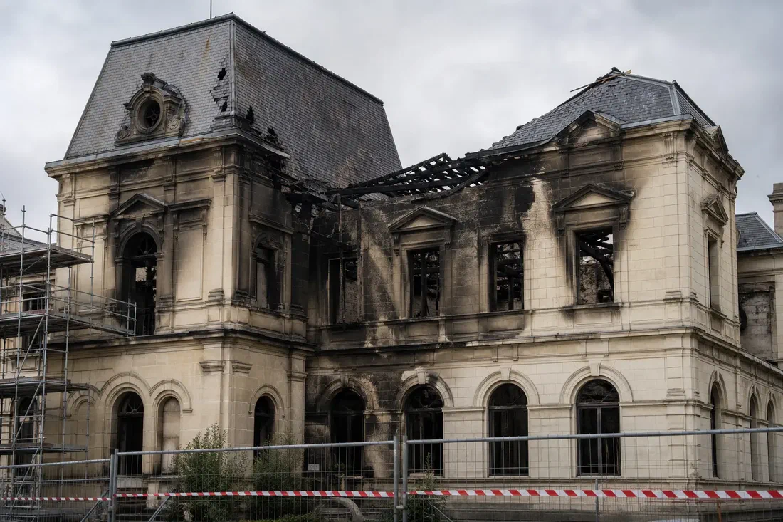 Illustration générée par IA d'une façade d'hôtel de ville français du XIXe siècle, toiture en partie effondrée et murs noircis par la suie, vue de jour