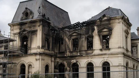 Illustration générée par IA d'une façade d'hôtel de ville français du XIXe siècle, toiture en partie effondrée et murs noircis par la suie, vue de jour