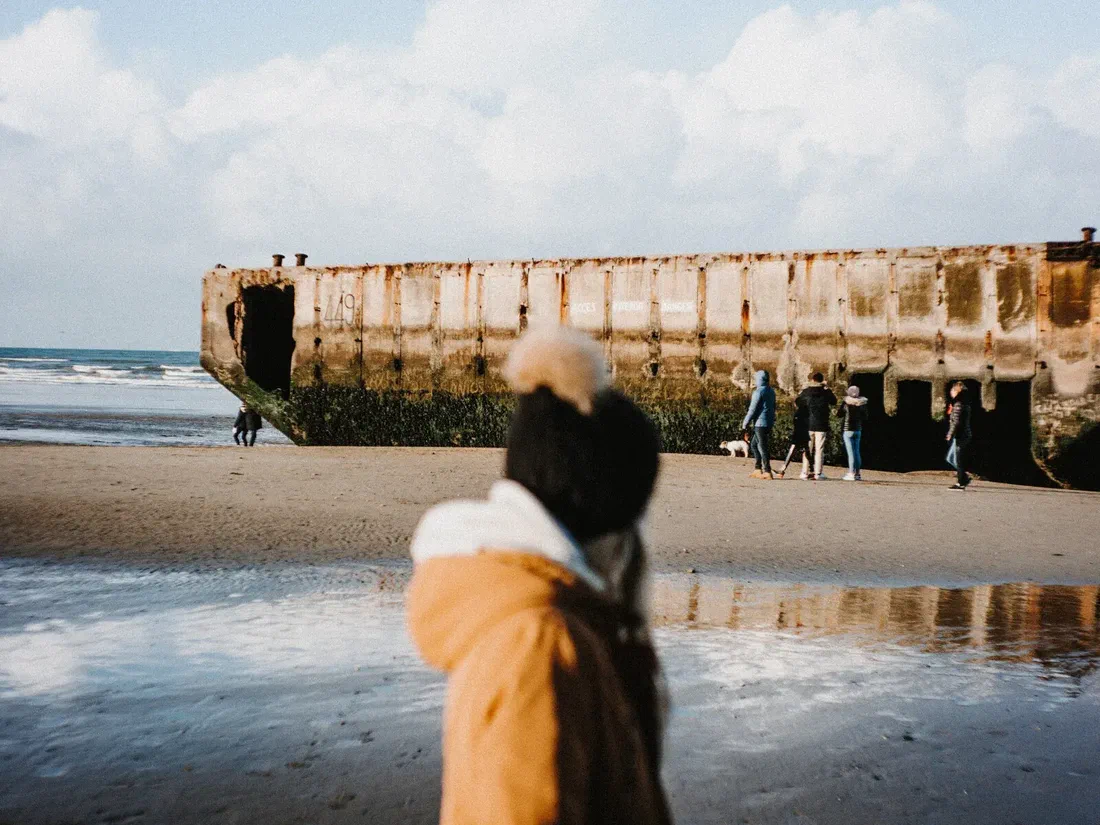 Des visiteurs face à un caisson de béton rouillé du port artificiel Mulberry, échoué sur la plage d&rsquo;Arromanches à marée basse