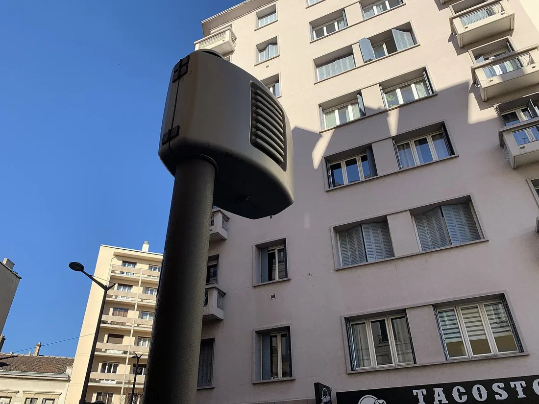 Radar automatique gris fixé sur un mât dans une rue de Lyon, devant un immeuble, sous un ciel bleu