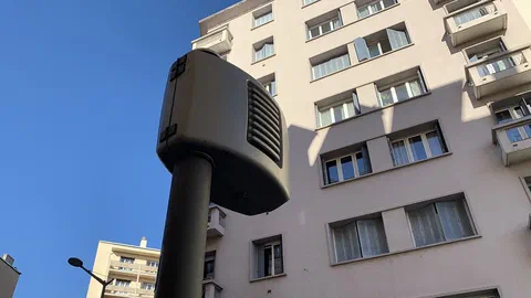 Radar automatique gris fixé sur un mât dans une rue de Lyon, devant un immeuble, sous un ciel bleu